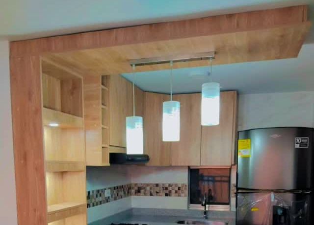 Cocina en madera con marco superior, lámparas colgantes y nevera
