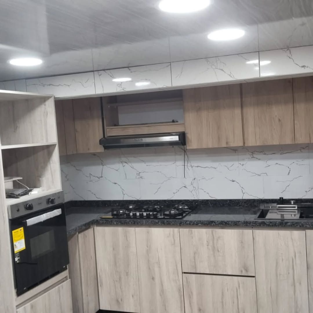 Cocina integral en madera clara con mesón oscuro y horno empotrado, instalada por Innovation In House
